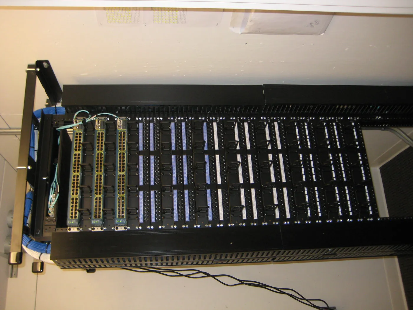 Overhead-mounted equipment rack with multiple Cat5e patch panels and labeled patch cords in a school telecom closet, viewed from above.