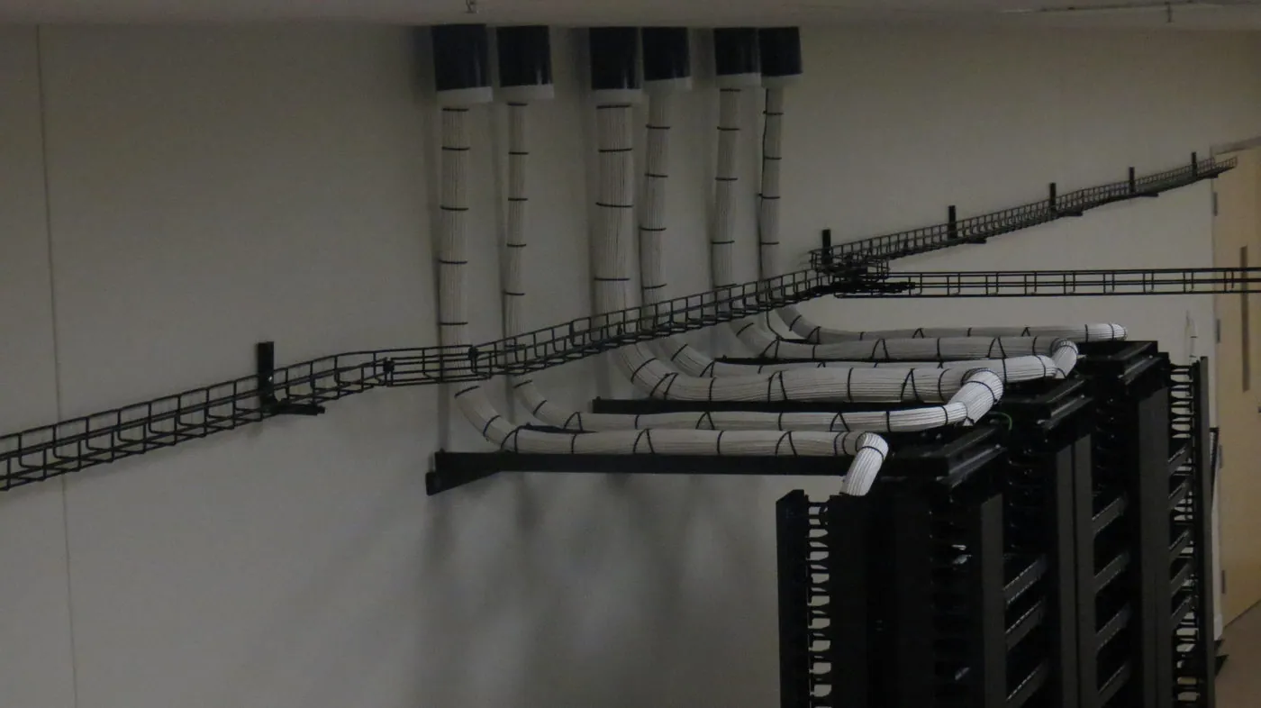Overhead cable tray carrying bundled white cabling above an open equipment rack, viewed from below in a stockroom ceiling.