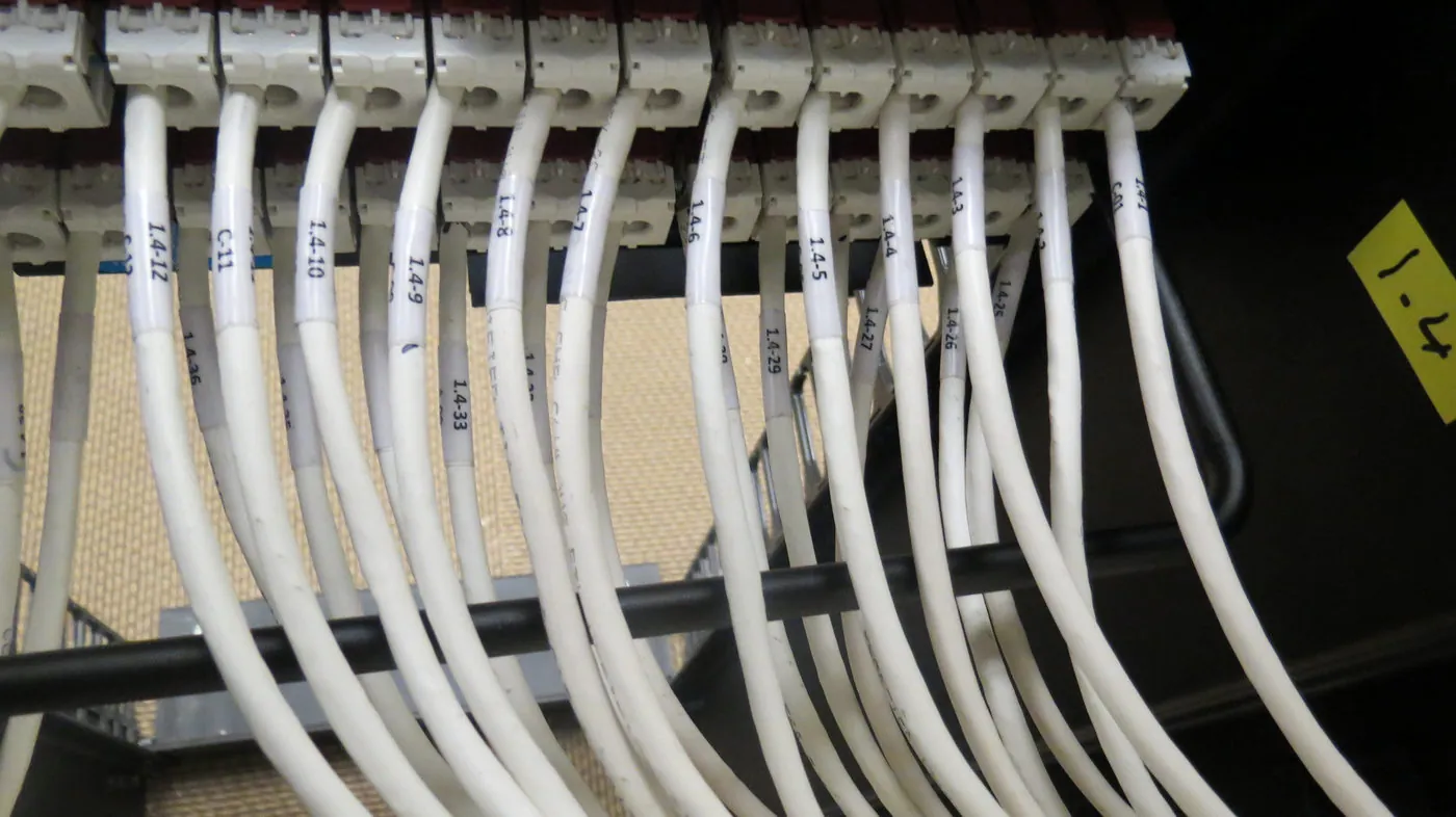 Close-up of individually labeled patch cords bundled and dressed at a wall-mounted termination block.