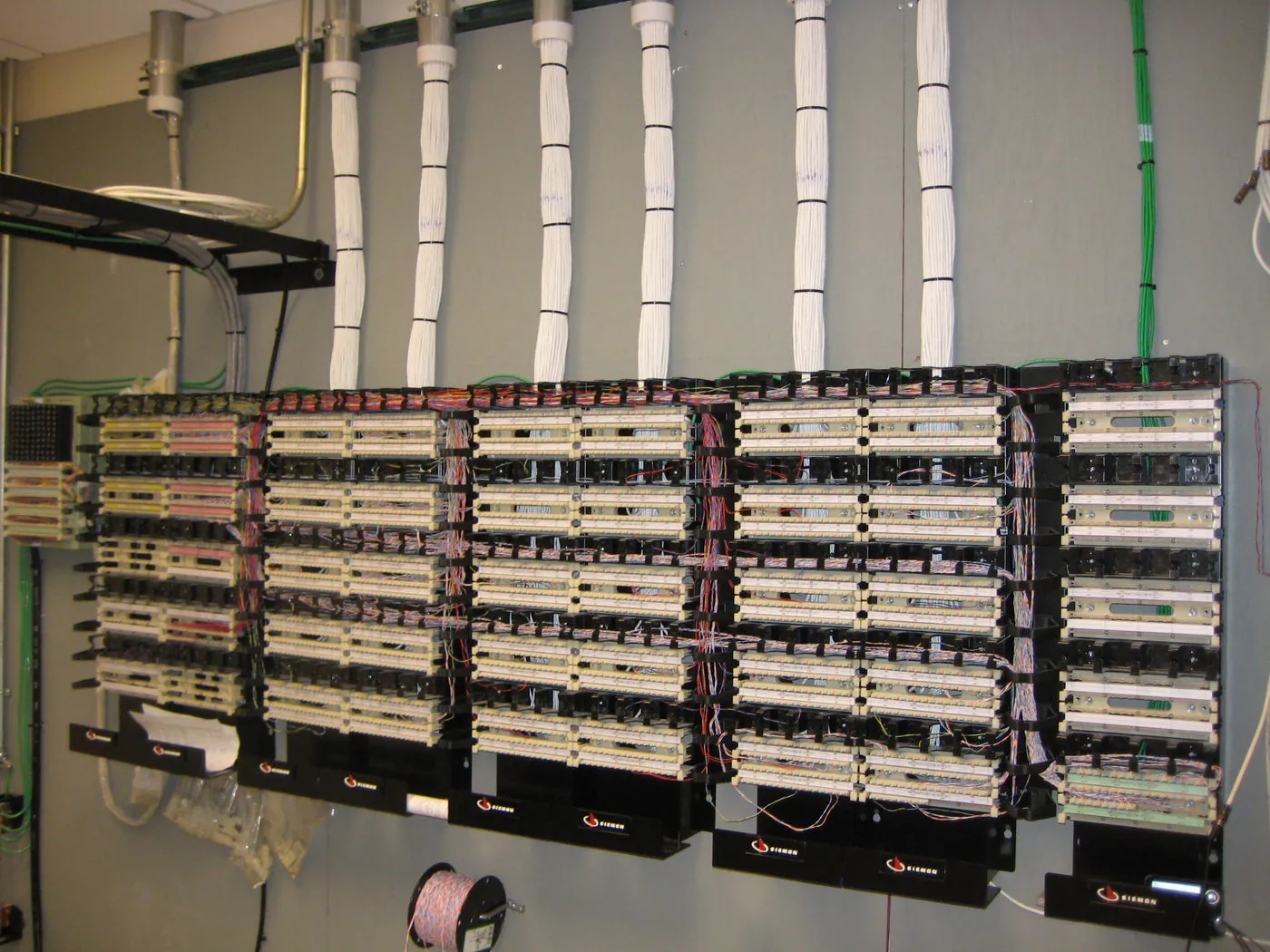 Close-up of labeled voice and data patch cords dressed and routed into a wall-mounted termination rack.