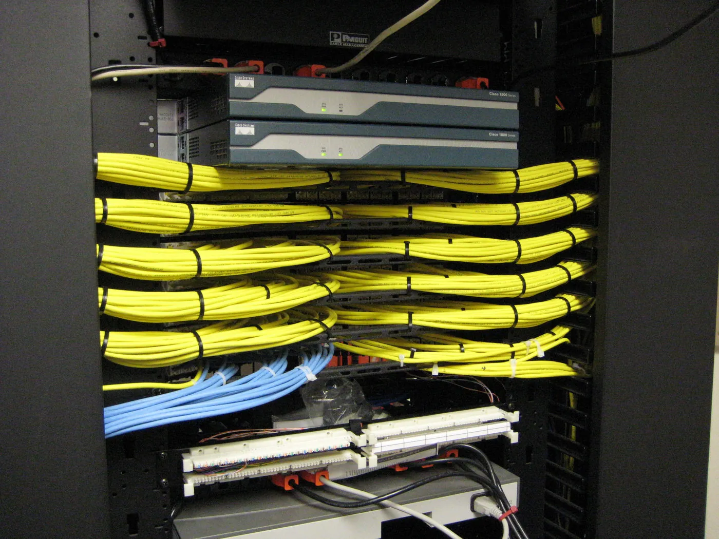 Equipment rack with two Cisco Systems routers mounted above rows of bundled yellow cabling feeding into a patch panel.