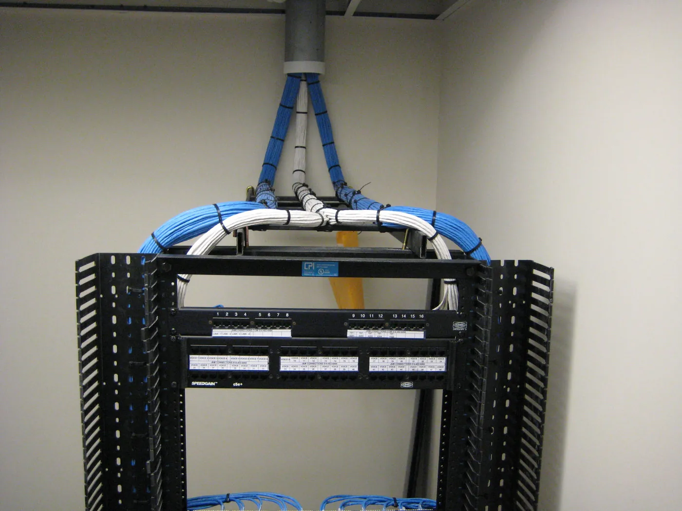 Technician's hand holding an open Leviton patch panel loaded with blue, yellow, and red RJ45 network jacks.