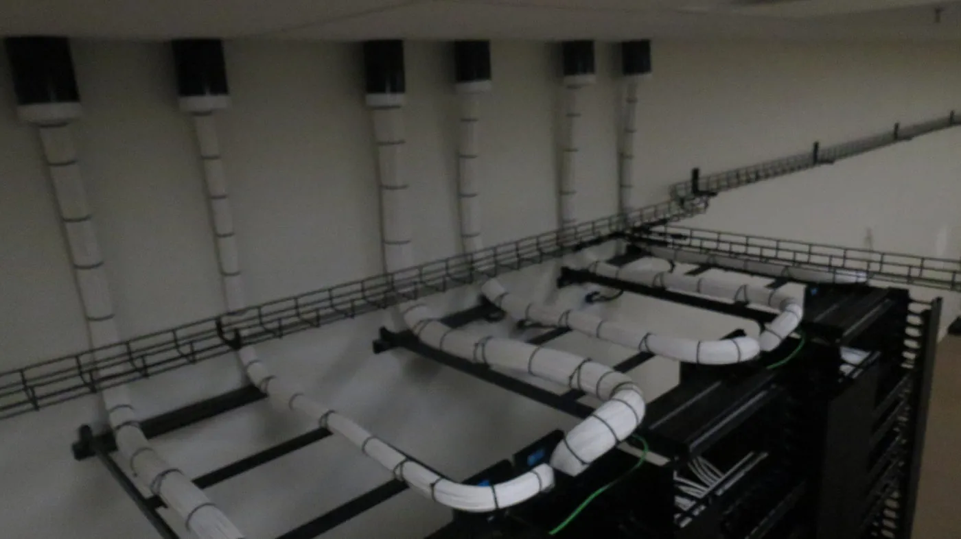 Overhead cable tray with six cable drops running from the ceiling down into open equipment racks.