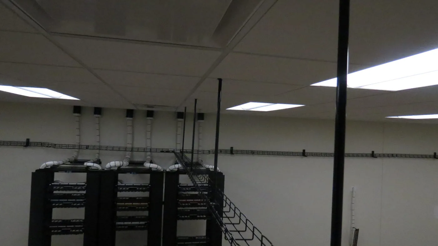 Ceiling-mounted cable tray with multiple cable drops feeding into open equipment racks below.