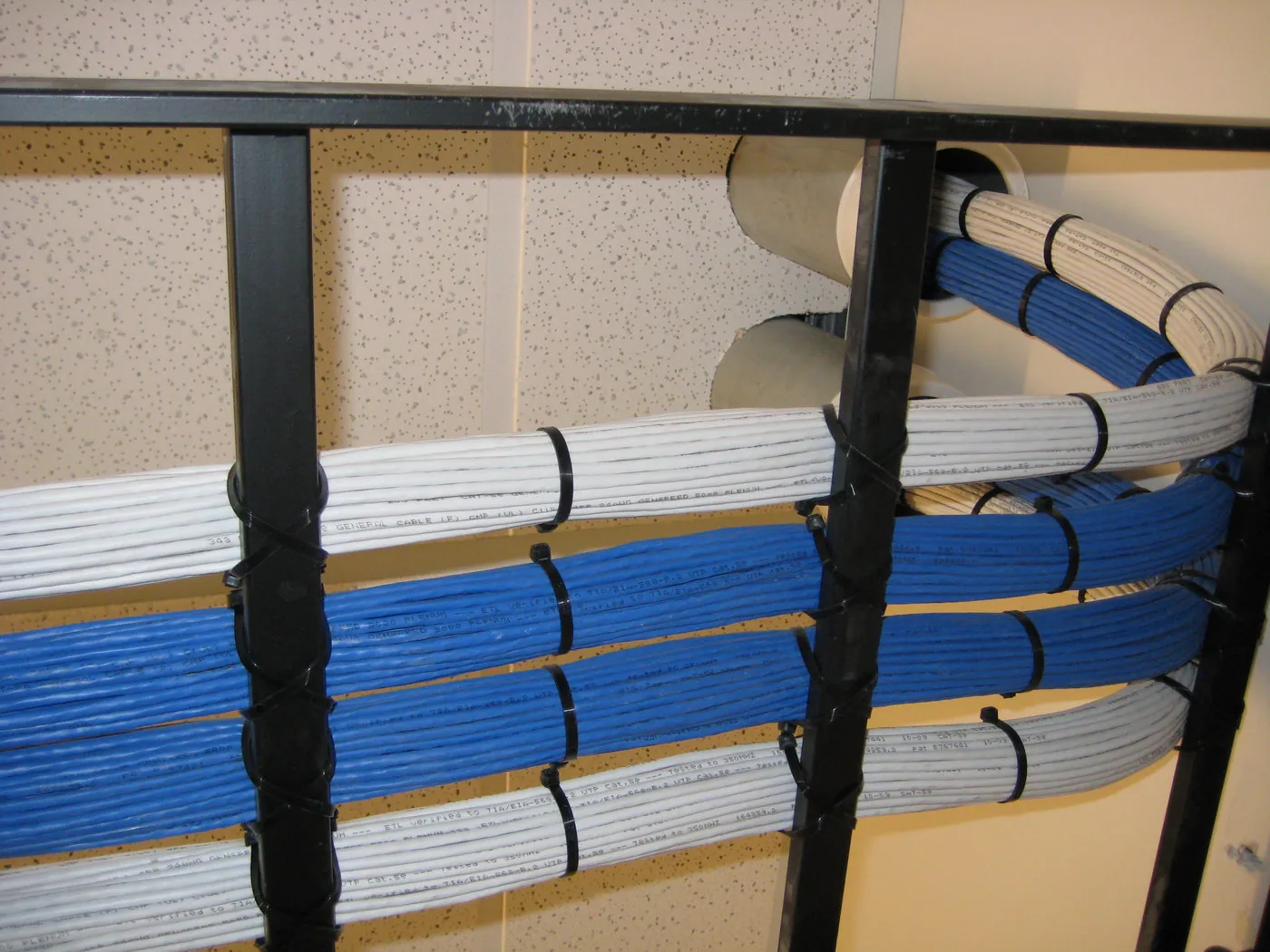Labeled blue and white Cat5e cable bundles secured to a cable rack and routed through a suspended ceiling toward equipment racks.